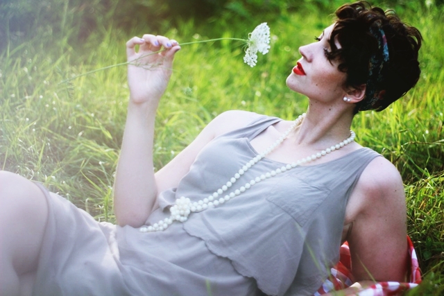 Vintage inspired outfit: Beige dress, long faux pearl necklace, vintage head scarf, red lipstick, sunny summer field