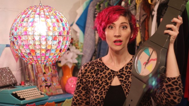 hannah rupp, the outfit repeater, with pink hair holds an oversized vintage thrifted swatch watch clock