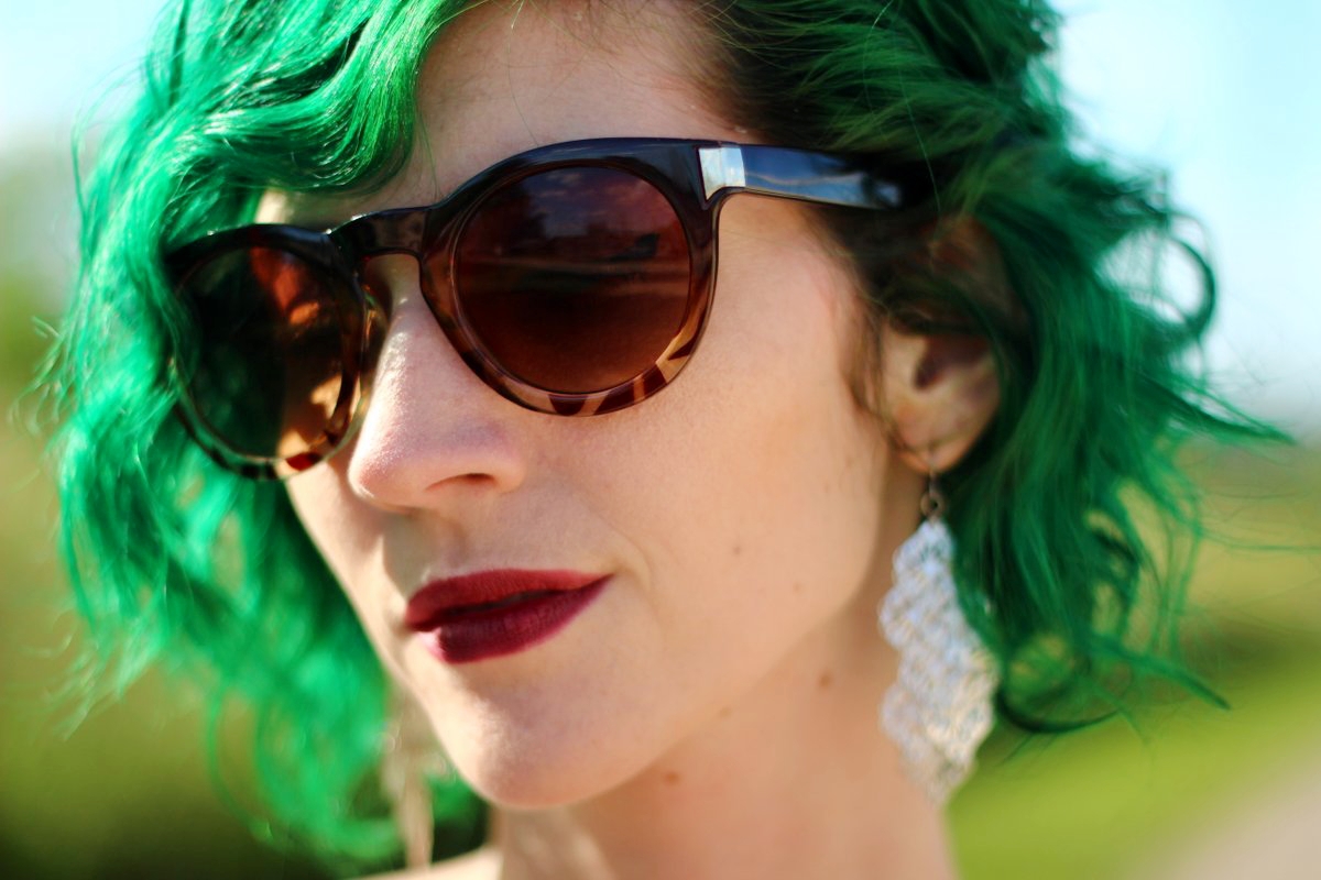 1 Top, 2 Music Festival Outfits | theoutfitrepeater.com a white female with green curly hair, dark lipstick, brown round tortoise shell sunglasses, and silver dangly earrings