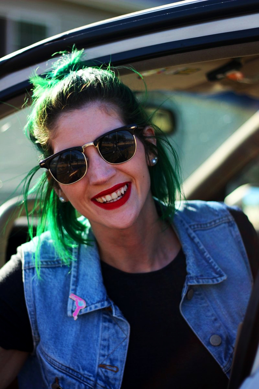 Road trip outfit details in a car: light wash denim vest, Darling Distraction enamel pins, ColourPop ultra matte lip color in Creeper, vintage black sunglasses