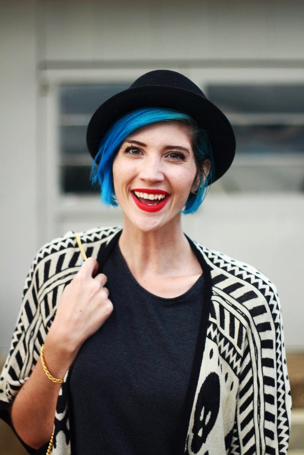 Outfit: Wearing a cardigan with a skull pattern, thrifted gray t-shirt dress, red purse, red lipstick, blue hair, black pork pie hat, black tights, black booties