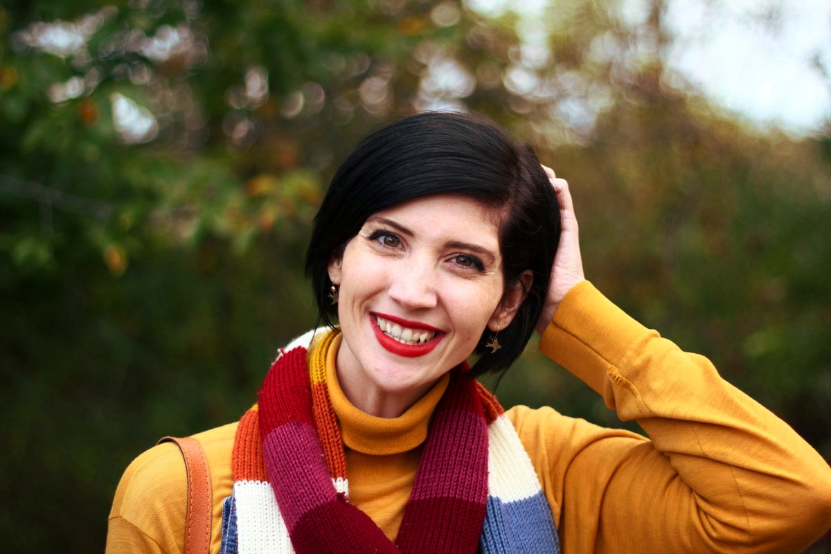 Outfit details: Mustard yellow turtleneck, denim overall dress, multi-colored striped scarf, red lipstick