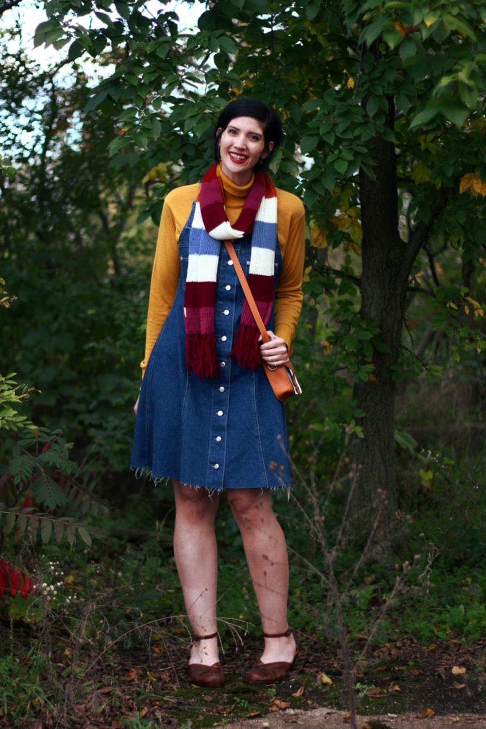 Outfit: Mustard yellow turtleneck, denim overall dress, multi-colored striped scarf, red lipstick, orange fox handbag, brown platforms