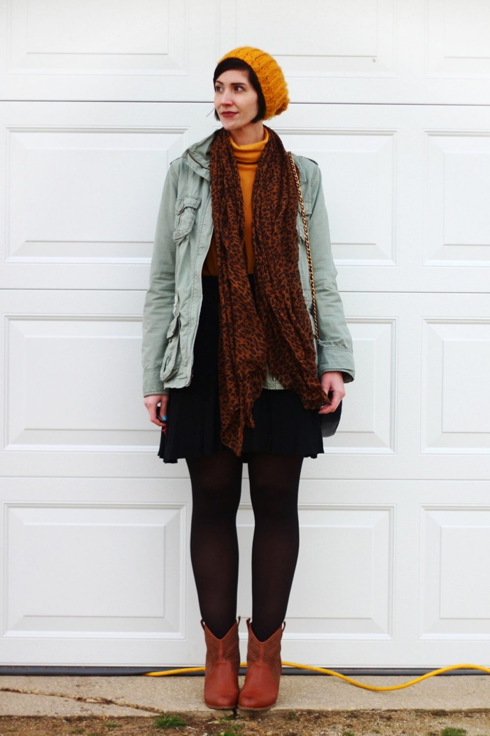Outfit: mustard yellow turtleneck, olive green utility jacket, leopard print scarf, yellow knit hat, black skater skirt, black tights, cognac colored boots, navy blue quilted purse