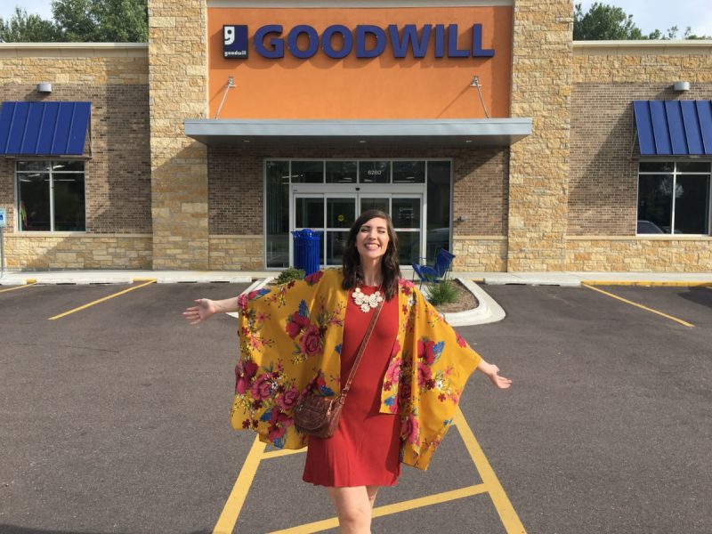 hannah rupp stands with open arms and a colorful outfit in front of an empty goodwill thrift store building