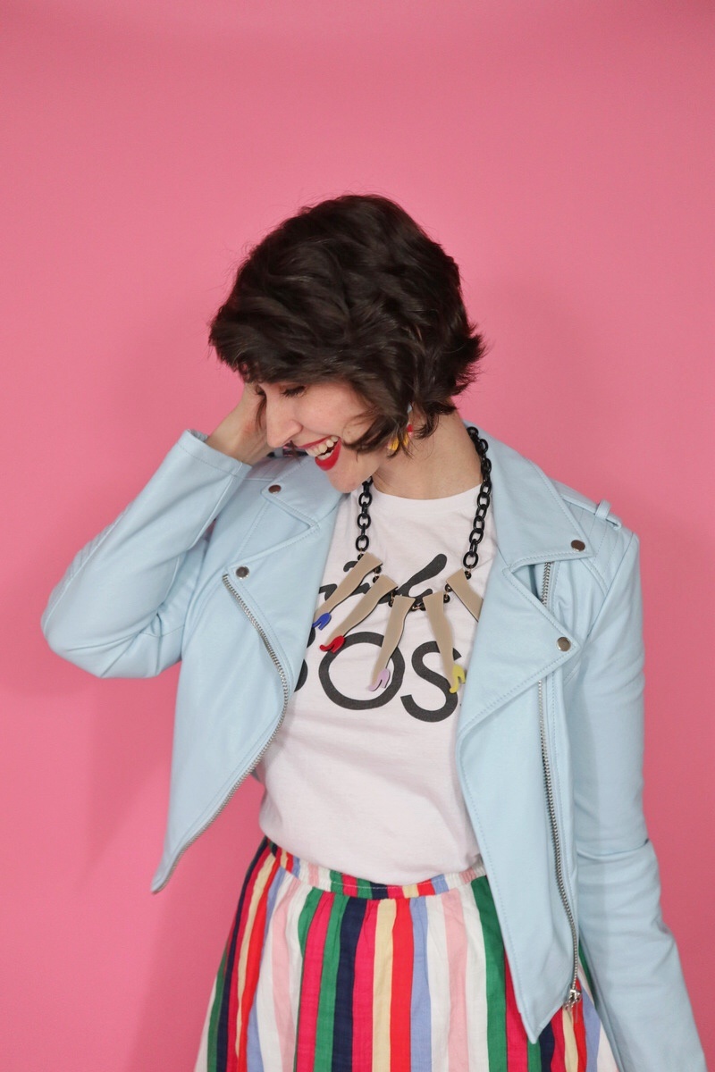 Hannah Rupp looking down wearing a white thrifted "girl boss" tee, statement necklace, and light blue leather moto jacket