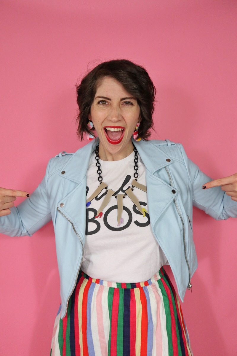 Hannah is wearing a thrifted graphic tee with a blue moto jacket on top, and a statement necklace