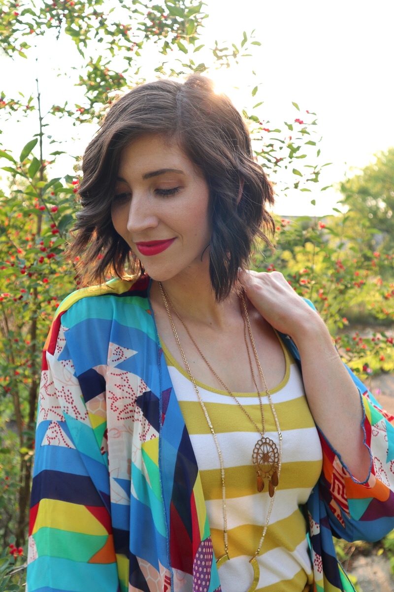 fashion blogger hannah rupp is smiling in an sunny outdoor setting. she's wearing a yellow striped tank top, yellow flouncy skirt, and a colorful kimono.
