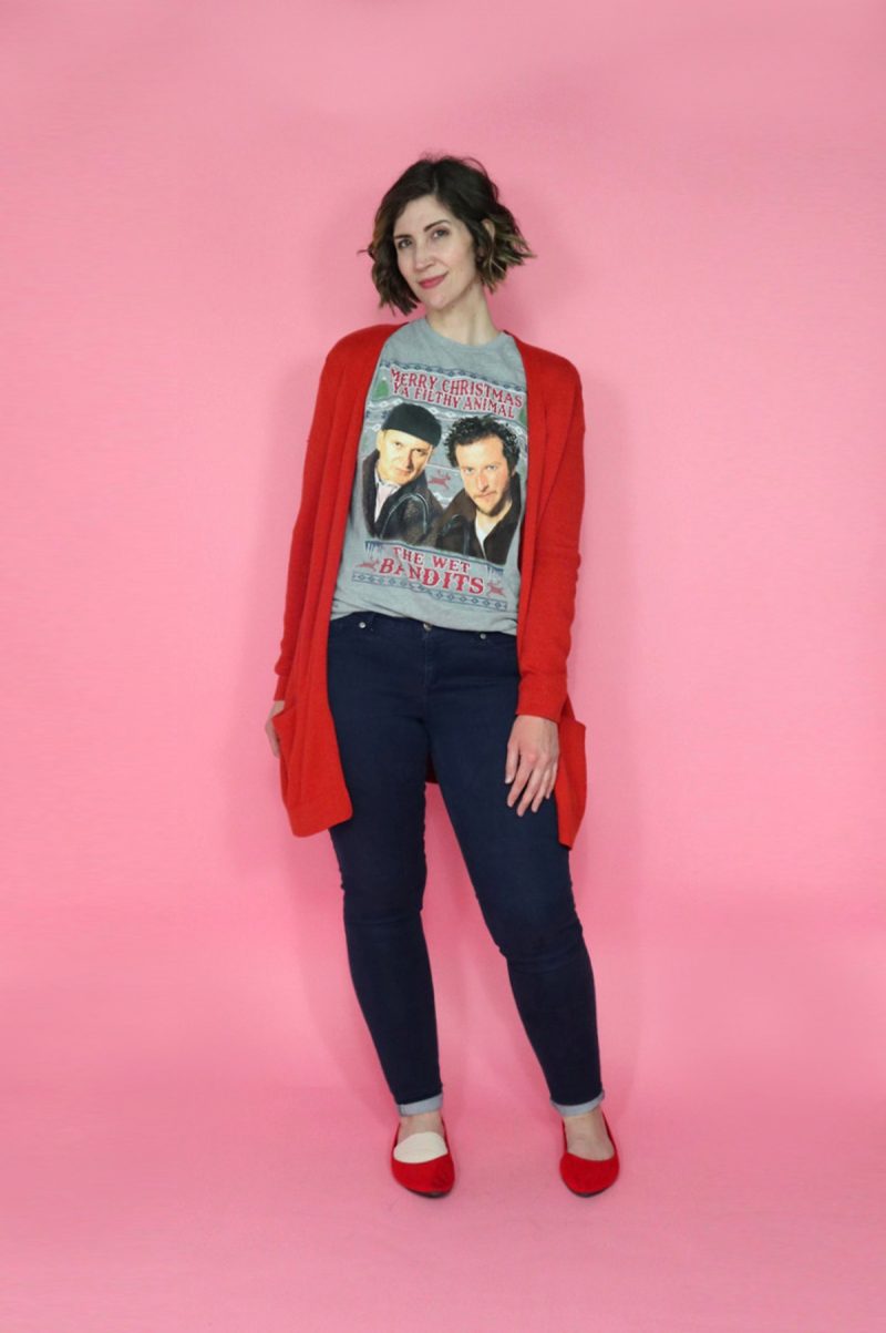hannah smiles mischievously while wearing a gray home along t-shirt, red cardigan, and blue pants