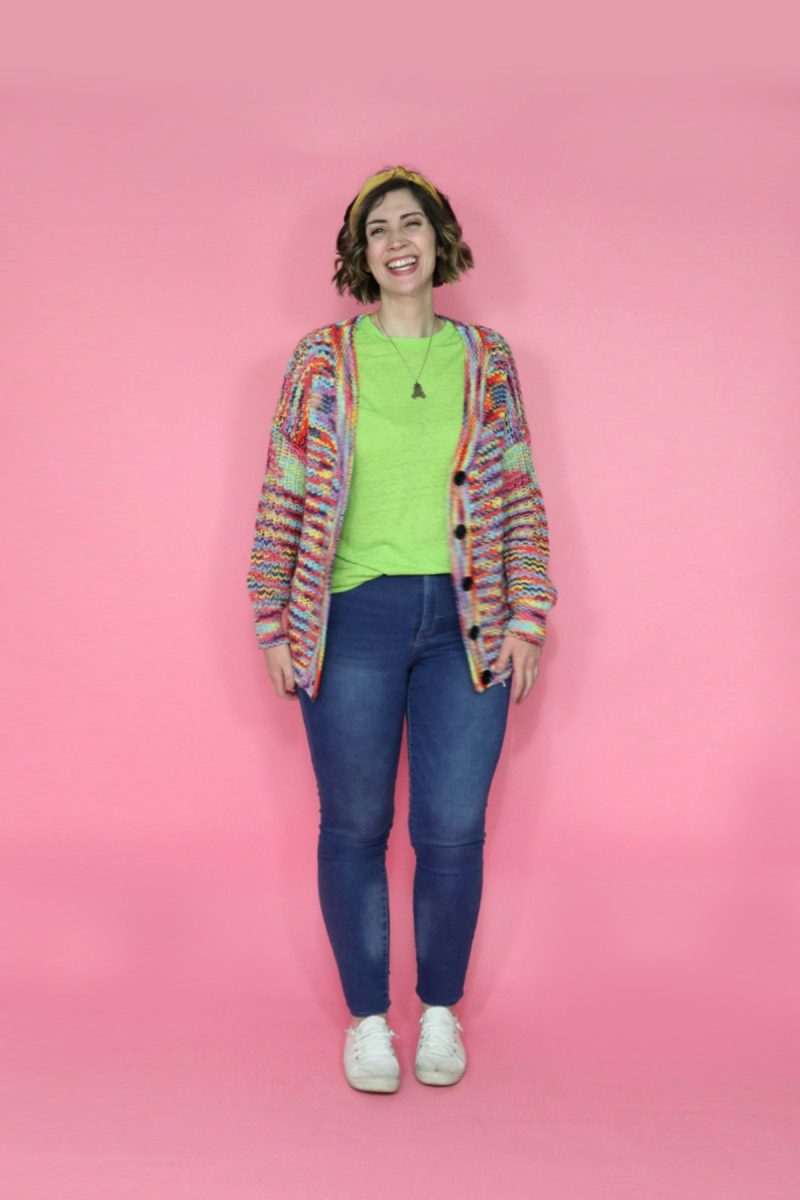 hannah is smiling in a lime green t-shirt, rainbow cardigan, and blue jeans