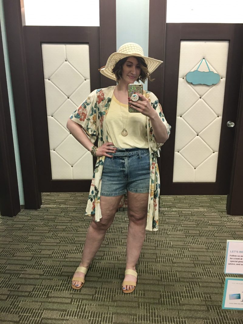 Outfit Photo Dump: What I Wore At Work (In A Clothing Store!) | www.theoutfitrepeater.com hannah is standing in front of a mirror. wearing a yellow tank top, floral kimono, light wash high waisted shorts, sandals, and a hat.
