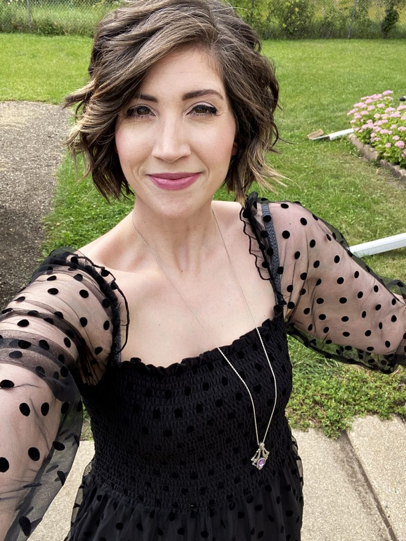 hannah is standing outside smiling in a long black maxi dress that has polka dots and puffed sleeves