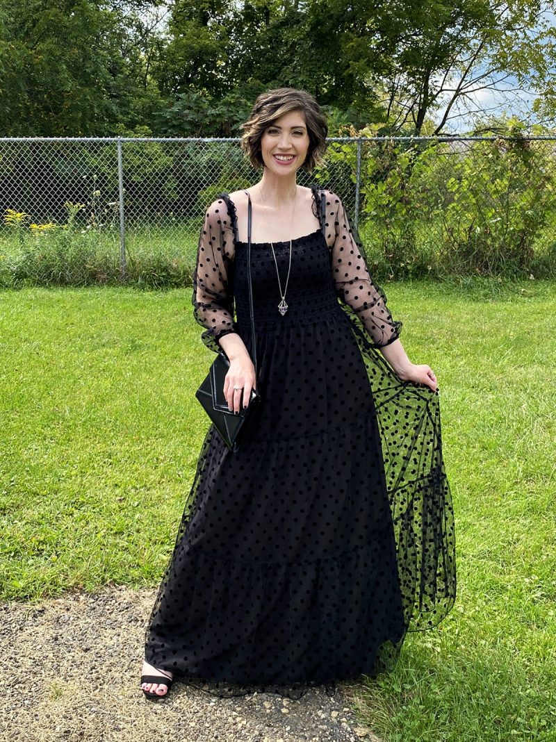 hannah is standing outside smiling in a long black maxi dress that has polka dots and puffed sleeves