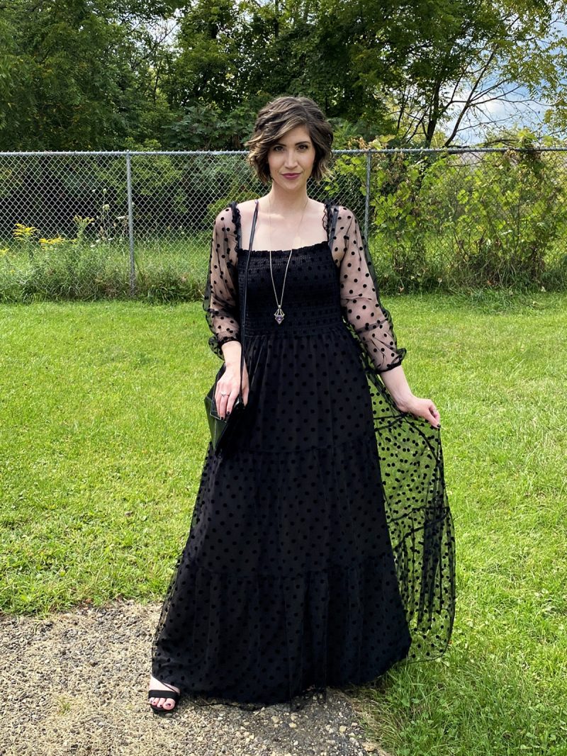 hannah is standing outside smiling in a long black maxi dress that has polka dots and puffed sleeves