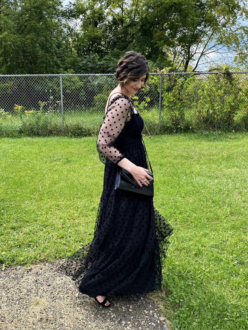 hannah is standing outside smiling in a long black maxi dress that has polka dots and puffed sleeves