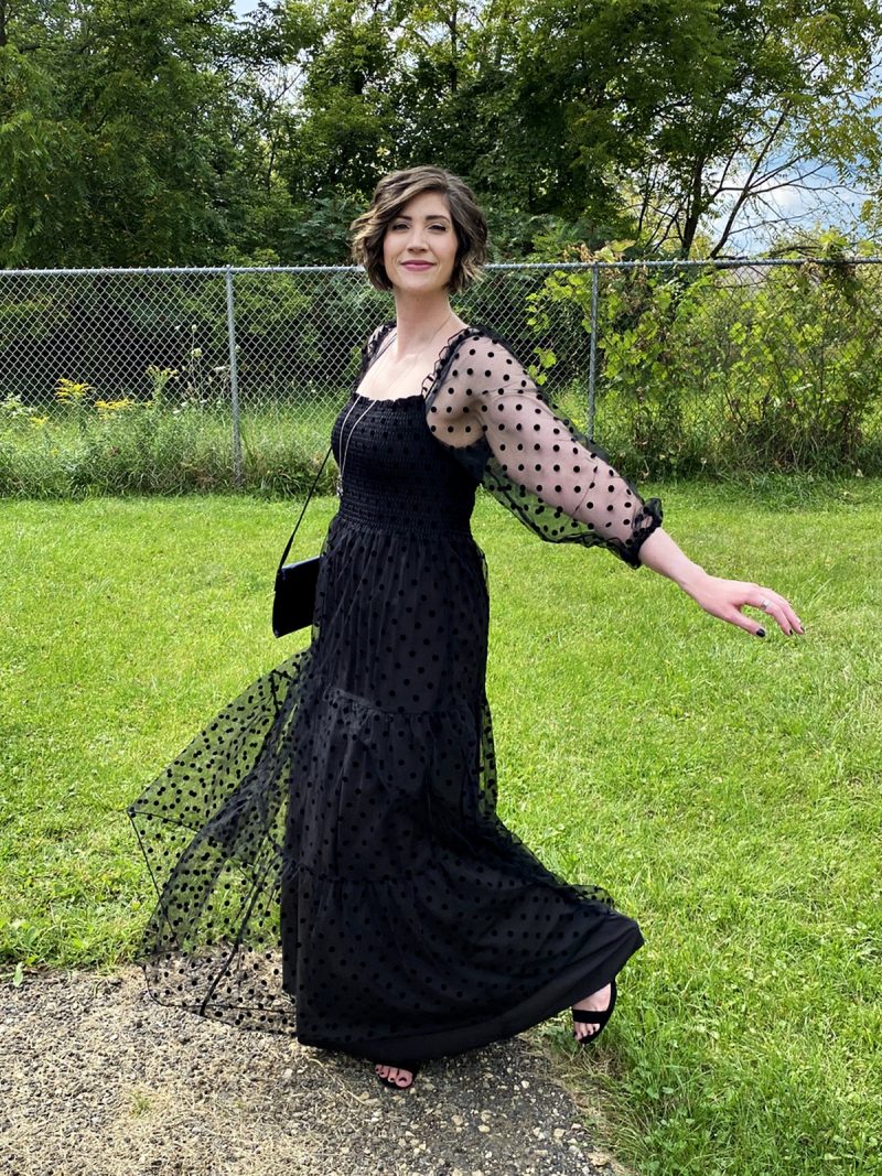 hannah is standing outside smiling in a long black maxi dress that has polka dots and puffed sleeves