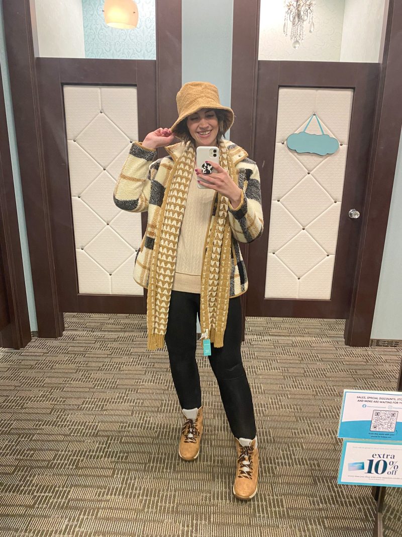 hannah is wearing maurices clothing - cream sweater, plaid jacket, mustard yellow scarf, black leggings, boots, and a furry hat