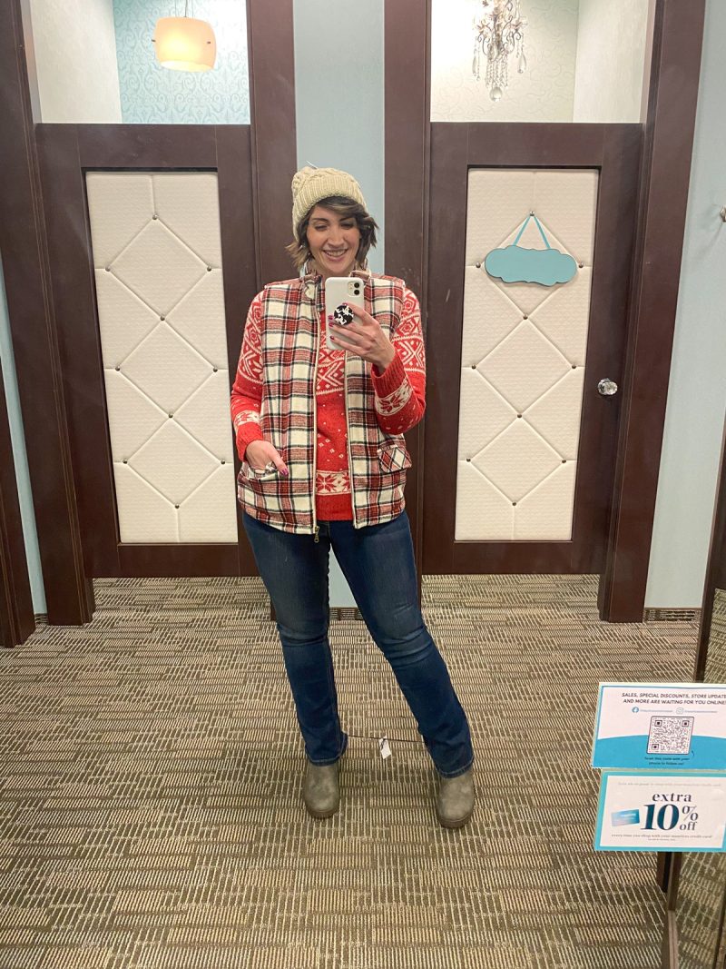 hannah is wearing maurices clothing - a red fair isle sweater, red plaid vest, bootcut jeans, brown boots, and a cream colored knit winter hat