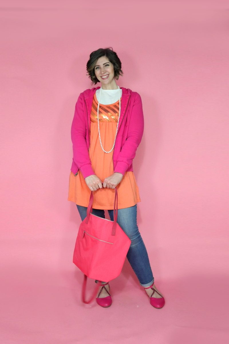 TikTok Outfit Challenge: My Followers Pick My Outfit For 1 Week | theoutfitrepeater.com hannah is posing in an orange mini dress layered over a white tee, on top is a pink zip up hoodie. she's wearing cuffed skinny jeans and pink accessories.