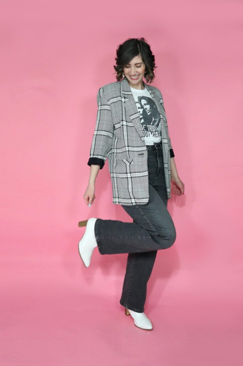 Jeans I Thrifted + 3 Ways I'm Styling Them | www.theoutfitrepeater.com hannah rupp is posing in a graphic tee shirt, oversized vintage plaid blazer, and high waisted thrifted jeans. she's kicking up her heel to reveal a white heeled boot.