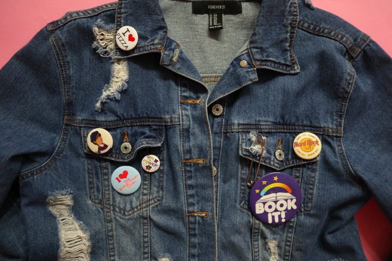 a distressed denim jacket with 90s themed pin, flair, buttons scattered around it