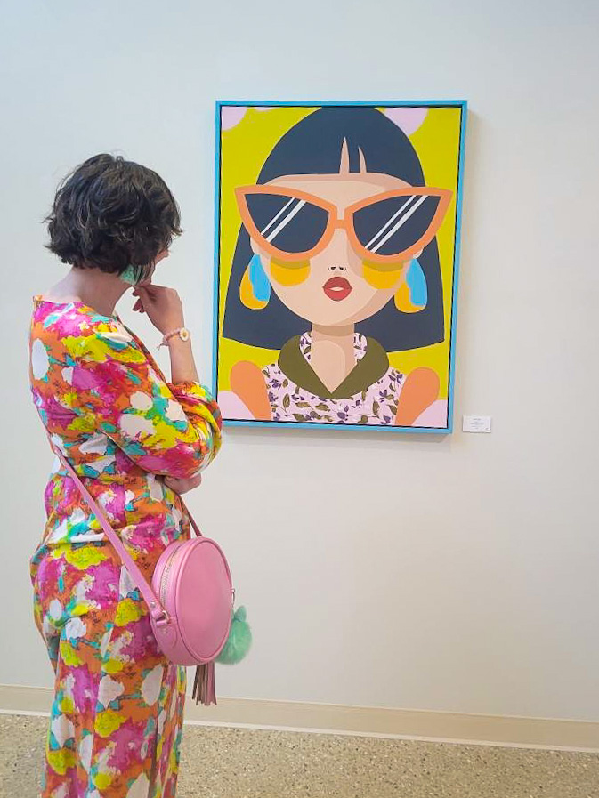 hannah is wearing a colorful maxi dress and pink crossbody purse. she's gazing at an Efflorescence by Emma Daisy painting at Monroe Arts Center in Monroe, Wisconsin