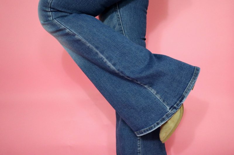 a pink background showing pair of light wash flared denim jeans and tan booties