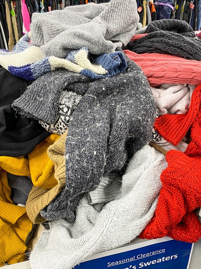 a pile of colorful sweaters in a bin at a thrift store