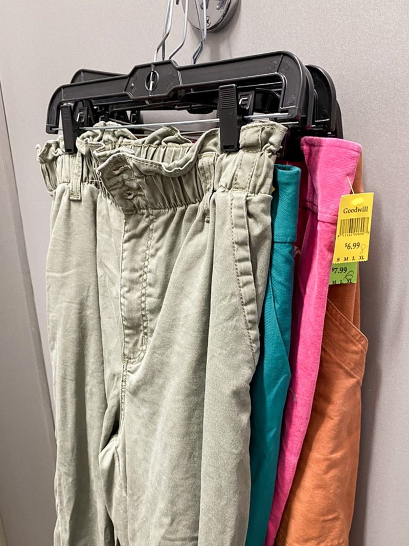 colorful pants on hangers hanging up in a thrift store fitting room