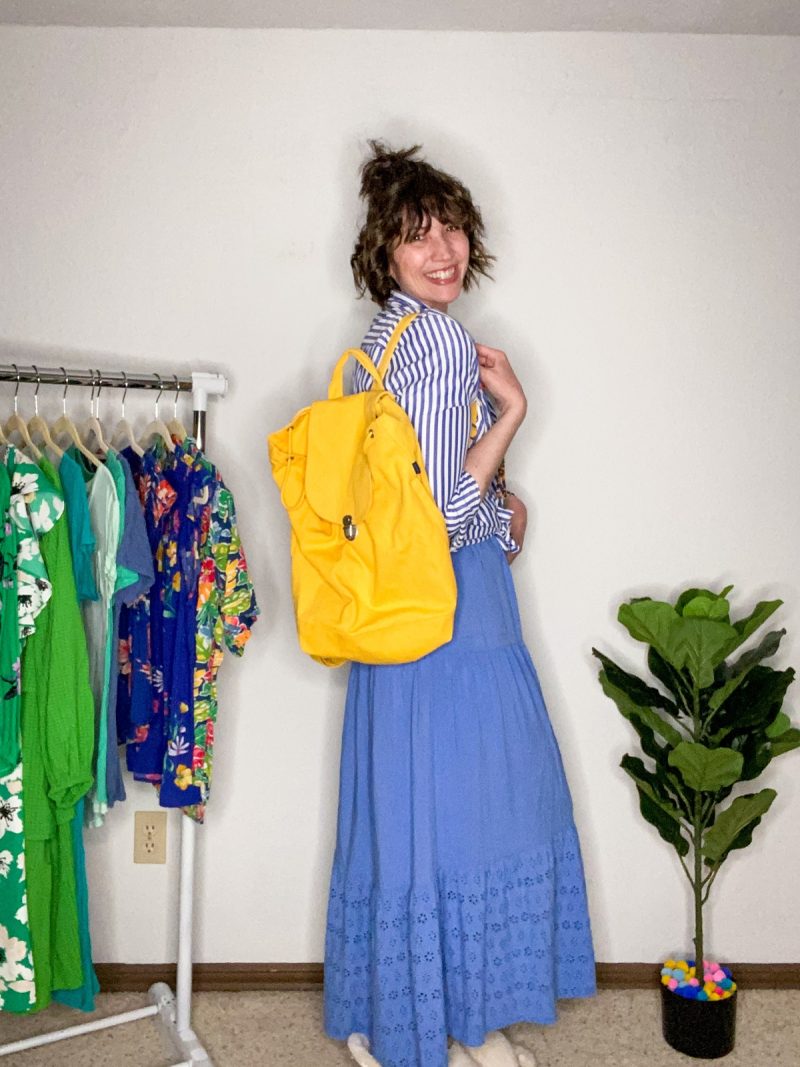 hannah is smiling and wearing a blue maxi dress and has a yellow baggu backpack slung on her shoulder from thredup
