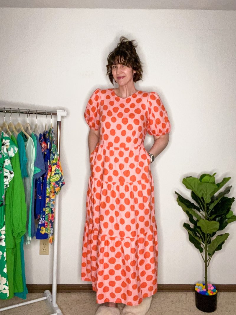 hannah is smiling and wearing a pink and orange polka dot floor length maxi dress from thredup