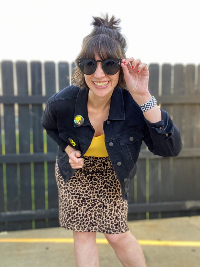 hannah rupp is a white female with short brown hair. she's wearing dark sunglasses, a black denim jacket, yellow tank top, and  leopard print skirt.