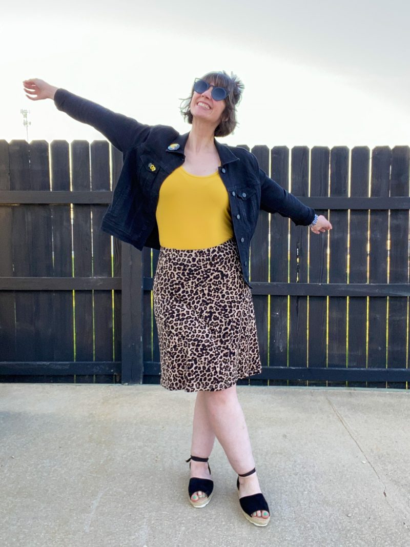 hannah rupp is a white female with short brown hair. she's wearing dark sunglasses, a black denim jacket, yellow tank top, leopard print skirt, and black sandals.