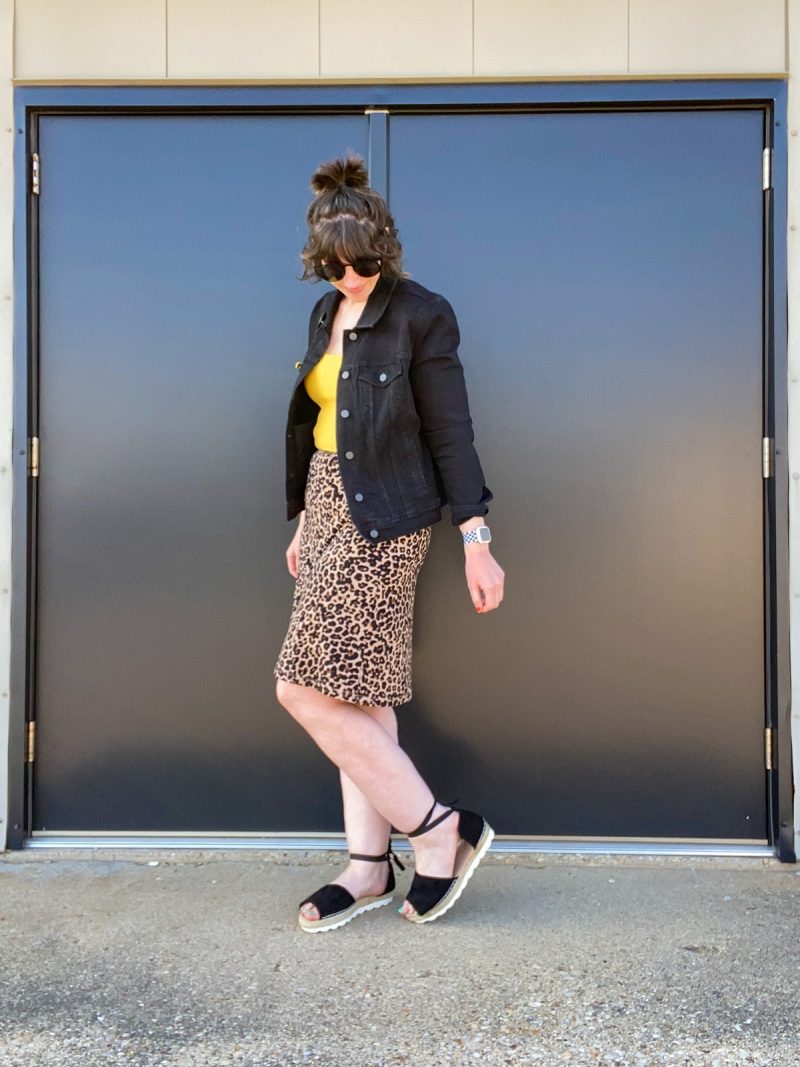 Wearing All Black Is Boring, Here's How To Make It Better | www.theoutfitrepeater.com hannah rupp is a white female with short brown hair. she's wearing dark sunglasses, a black denim jacket, yellow tank top, leopard print skirt, and black sandals.