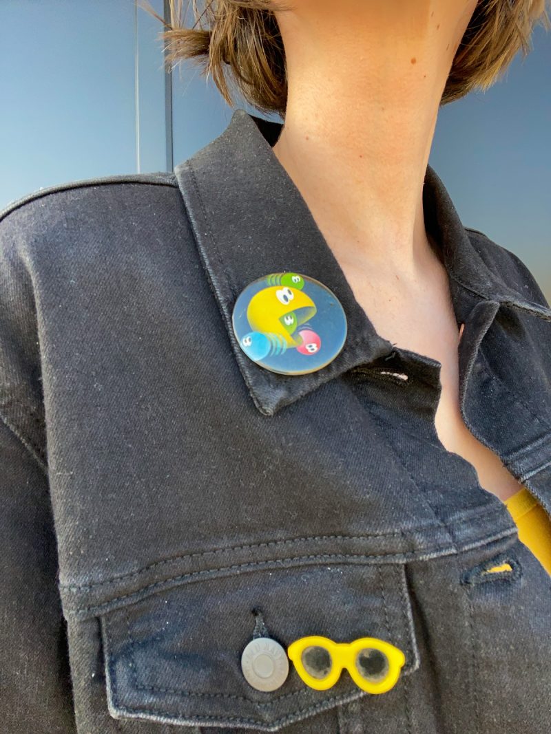 Wearing All Black Is Boring, Here's How To Make It Better | www.theoutfitrepeater.com a close-up of a denim jacket with a vintage pac-man button and yellow sunglasses pin
