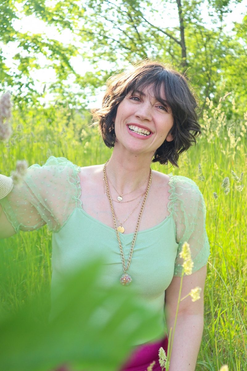 hannah rupp is in a bright, green field. she's wearing a mint green blouse and gold jewelry.