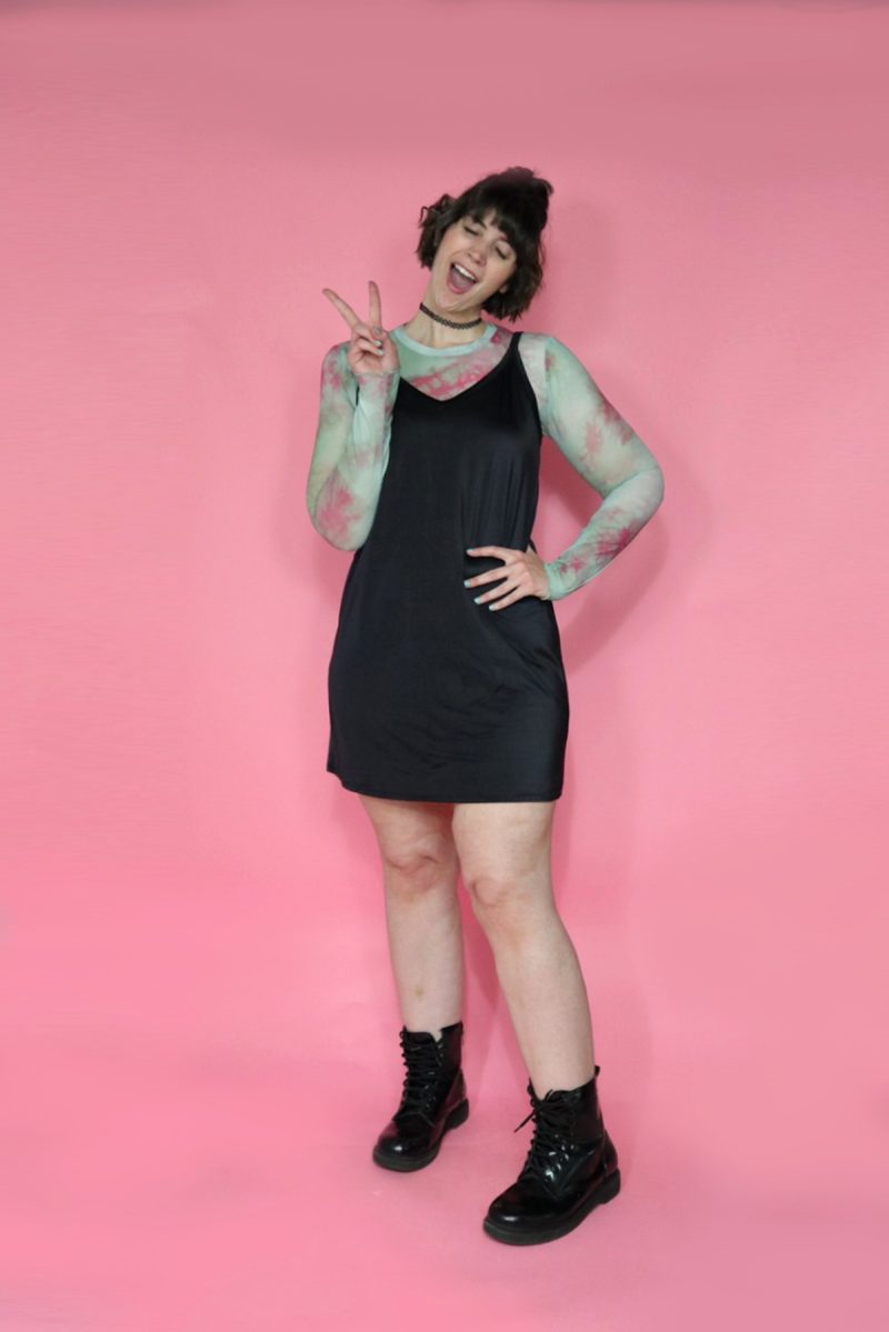 A thredUP Summer Thrift Haul | What I'm Keeping + Returning | www.theoutfitrepeater.com hannah is giving a peace sign in front of a pink background. she's wearing a multicolor long sleeve shirt under a black slip dress, and black doc marten boots.