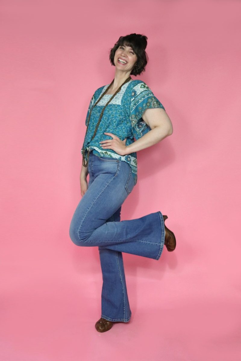 A thredUP Summer Thrift Haul | What I'm Keeping + Returning | www.theoutfitrepeater.com hannah is smiling in front of a pink background. she's wearing a blue boho blouse, high waisted flared denim, and brown platform shoes.