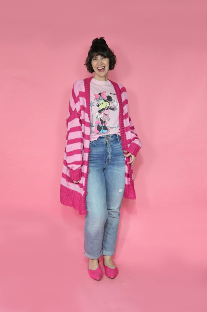A thredUP Summer Thrift Haul | What I'm Keeping + Returning | www.theoutfitrepeater.com hannah is smiling in front of a pink background. she's wearing a pink minnie mouse tee, oversized pink striped cardigan, high waisted jeans, and pink ballet flat shoes.