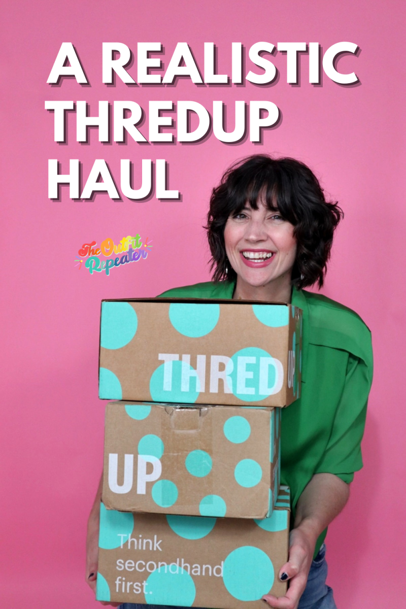 a white female with short curly brown hair is smiling in front of a pink background. she's wearing wearing and holding a stack of shipping boxes.