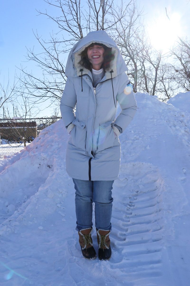 1 Winter Coat, 3 Ways | www.theoutfitrepeater.com hannah is smiling outside in front of a pile of snow. she's wearing a blue puffer coat, jeans, and snow boots.