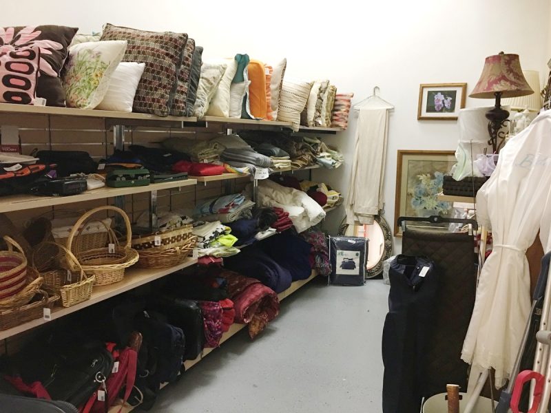 the bedding section of a thrift store filled with shelves of pillows, baskets, and sheets