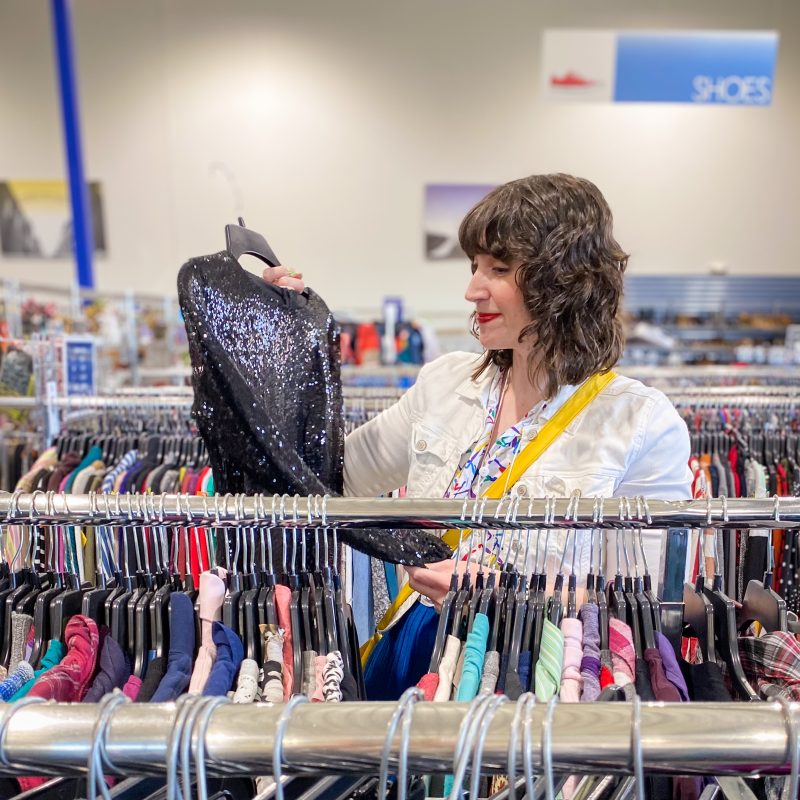 white female holding up a black sequined top in a thrift store