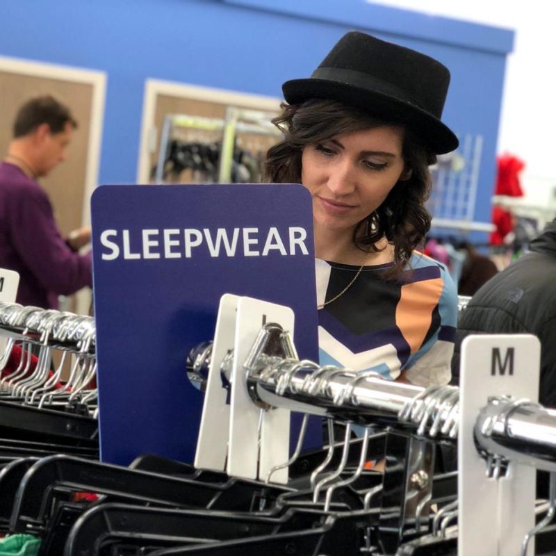 a white female in a black hat looks at a rack of sleepwear in a thrift store