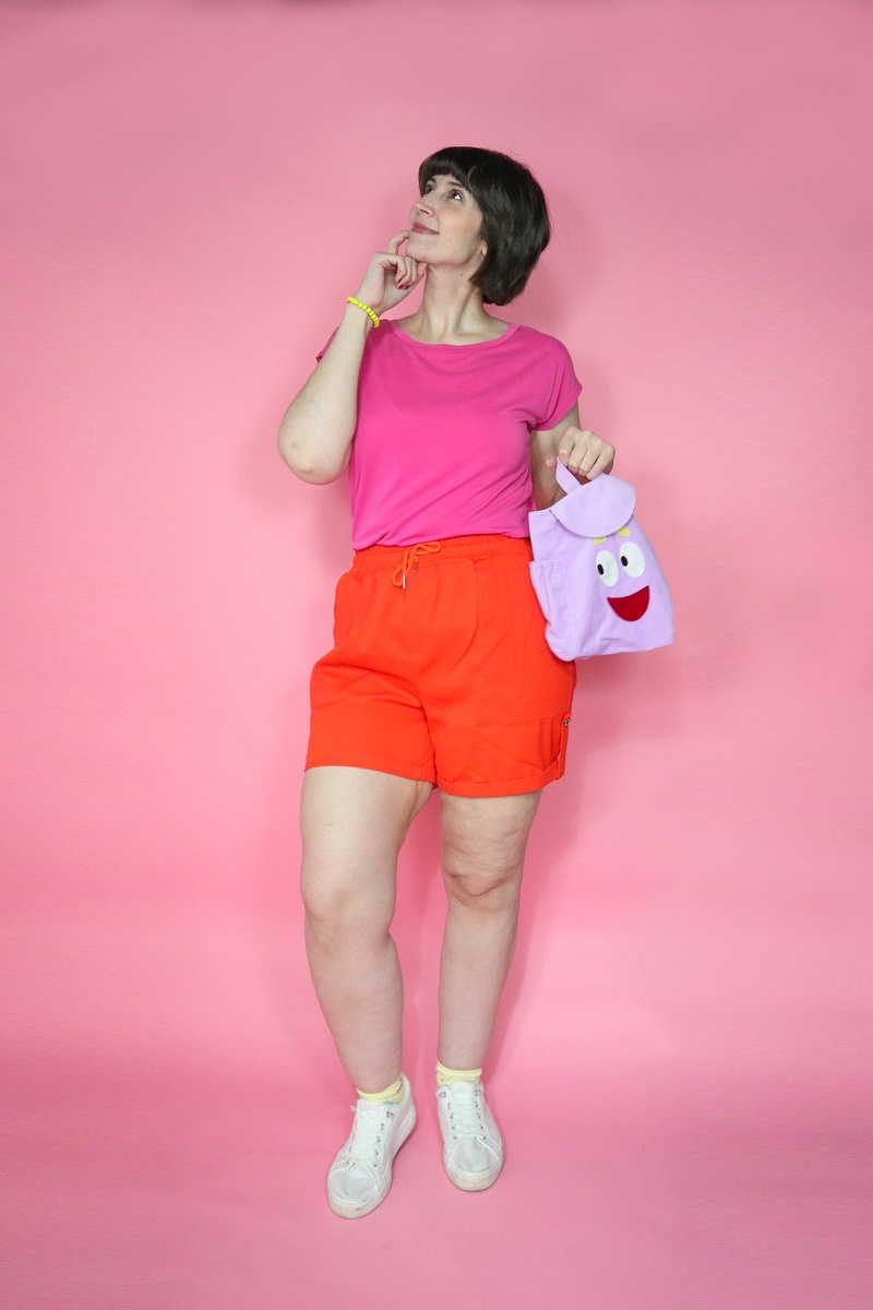 A Legendary Dora the Explorer Halloween Costume | www.theoutfitrepeater.com a dora the explorer halloween costume portrayed by a white millennial women with short brown bob hair, pink t-shirt, orange shorts, and purple backpack