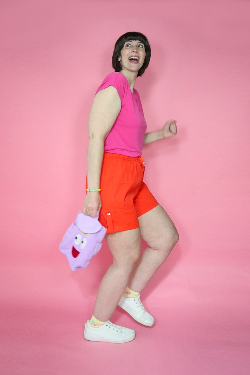 A Legendary Dora the Explorer Halloween Costume | www.theoutfitrepeater.com a dora the explorer halloween costume portrayed by a white millennial women with short brown bob hair, pink t-shirt, orange shorts, and purple backpack