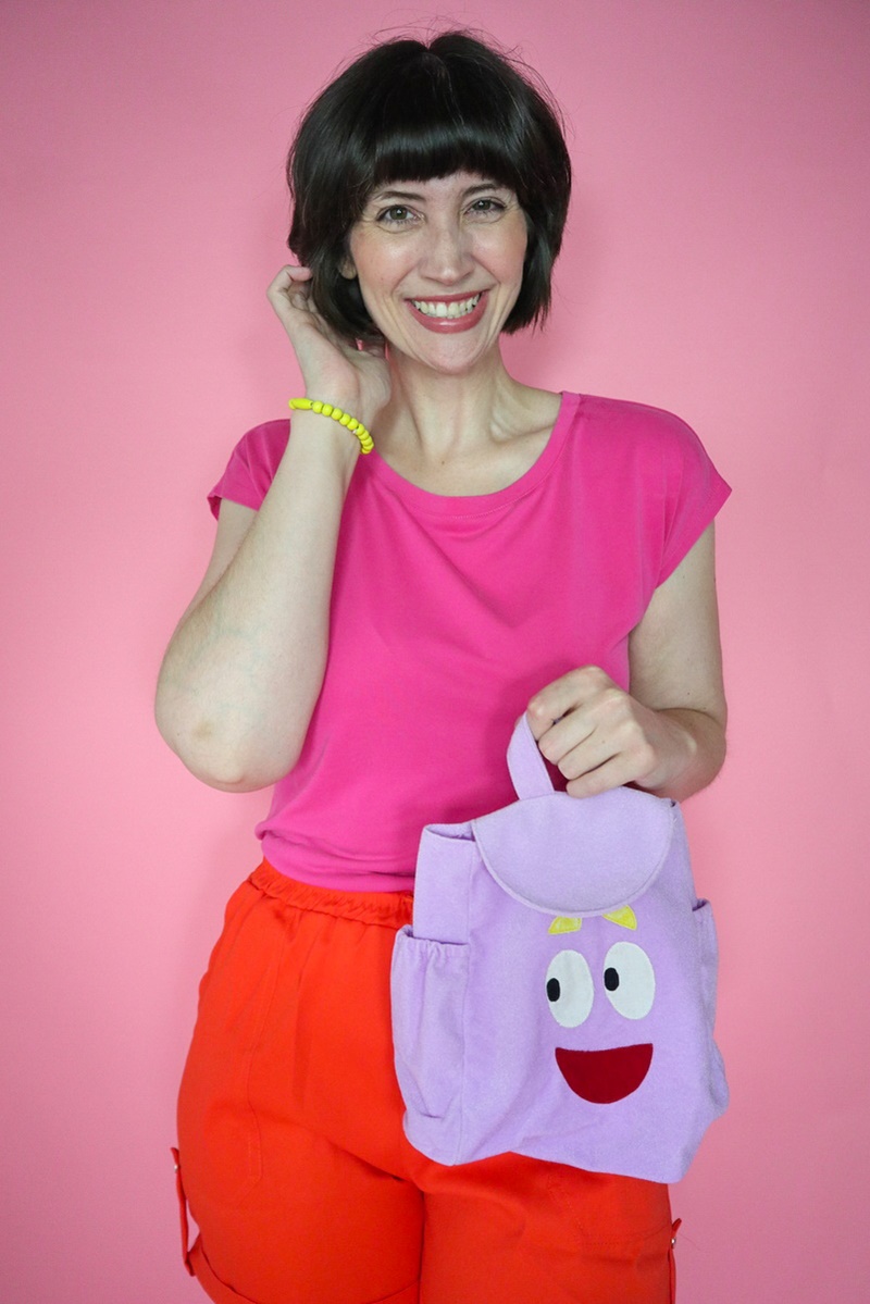A Legendary Dora the Explorer Halloween Costume | www.theoutfitrepeater.com a dora the explorer halloween costume portrayed by a white millennial women with short brown bob hair, pink t-shirt, orange shorts, and purple backpack