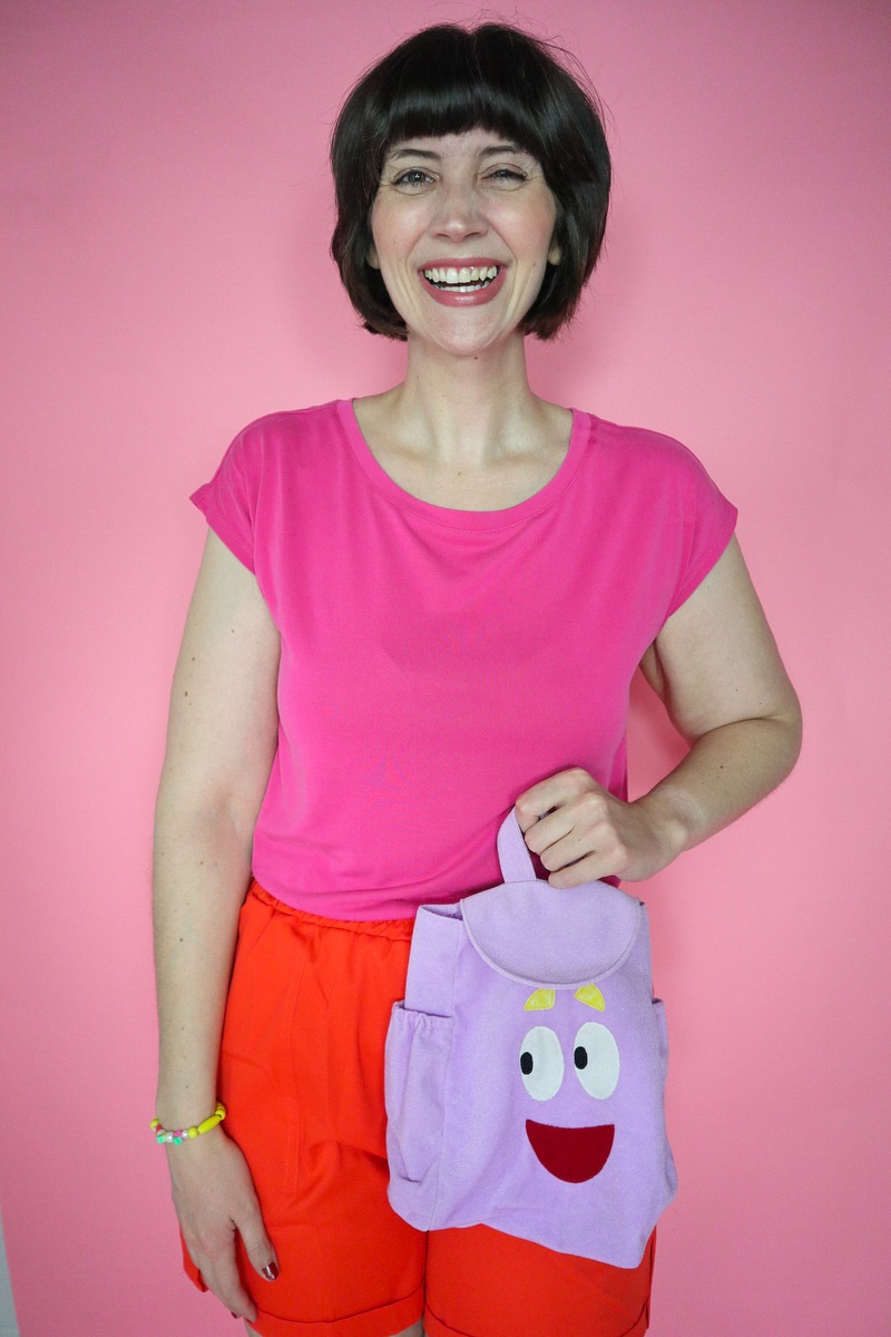 A Legendary Dora the Explorer Halloween Costume | www.theoutfitrepeater.com a dora the explorer halloween costume portrayed by a white millennial women with short brown bob hair, pink t-shirt, orange shorts, and purple backpack