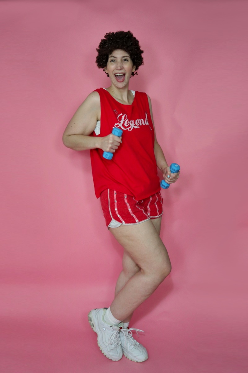 thrifted richard simmons halloween costume red tank top, tiny striped dolphin shorts, curly hair, and white sneakers