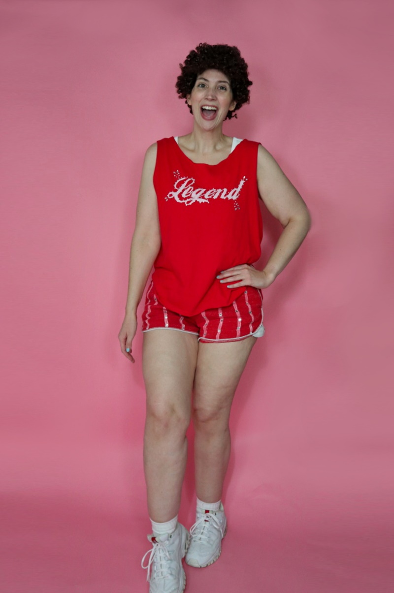 thrifted richard simmons halloween costume red tank top, tiny striped dolphin shorts, curly hair, and white sneakers